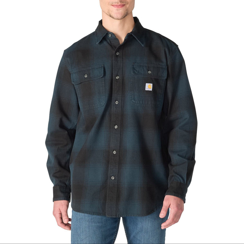 Load image into Gallery viewer, A man wearing a dark navy Carhartt long-sleeve plaid button-up shirt with blue jeans, photographed against a solid white background.
