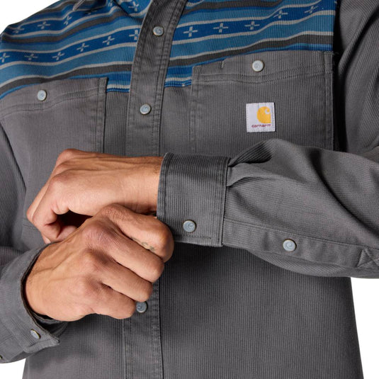 Close-up of a person wearing a gray shirt with a Carhartt logo, adjusting the sleeve.