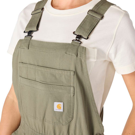 Person wearing green shortalls with a visible Carhartt logo on a white background