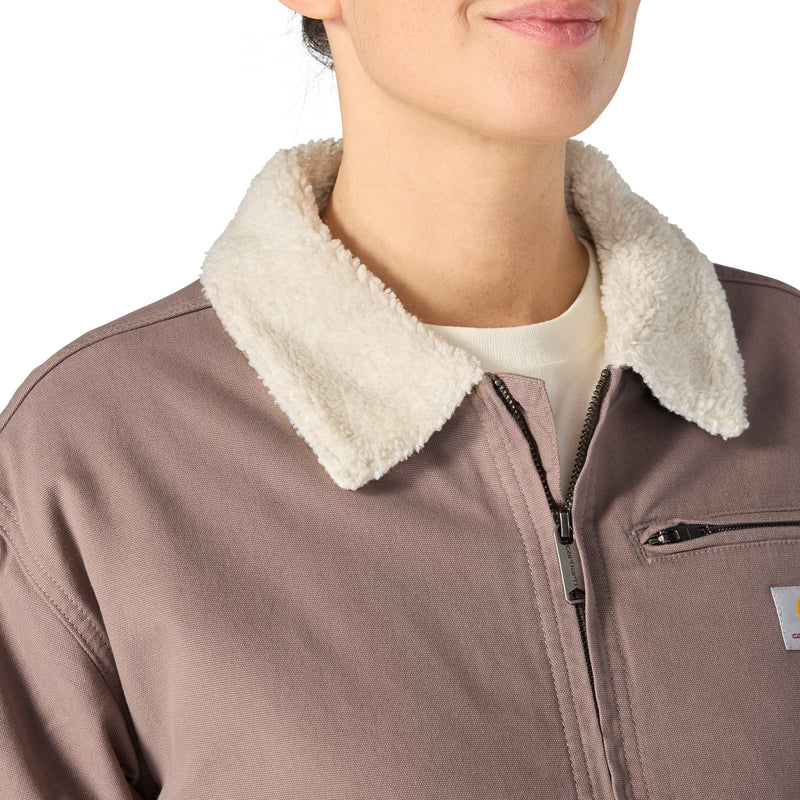 Load image into Gallery viewer, Close-up of a person wearing a taupe-brown work jacket with a thick cream sherpa collar, a black zipper, and a small Carhartt logo patch on the chest pocket.
