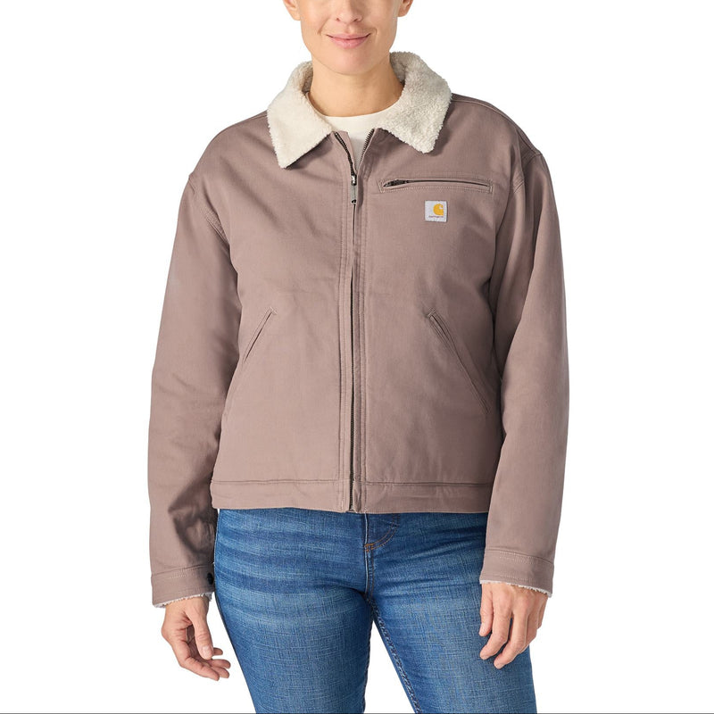 Load image into Gallery viewer, A woman modeling a Carhartt work jacket with a light beige sherpa collar, featuring a front zipper, chest pocket, and blue jeans against a plain white background.
