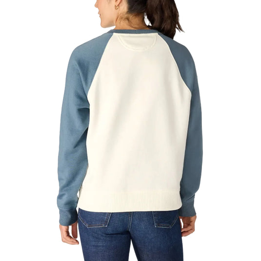 A woman shown from the back wearing a raglan-style crewneck sweatshirt with an off-white body and muted blue sleeves, paired with blue jeans, against a light gray studio background.