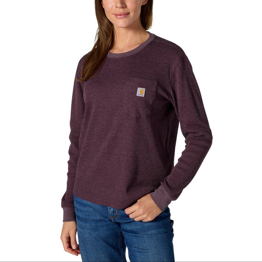 A woman modeling a dark heathered plum long-sleeve crewneck shirt with a small Carhartt logo patch on the left chest, paired with blue jeans against a plain white background.