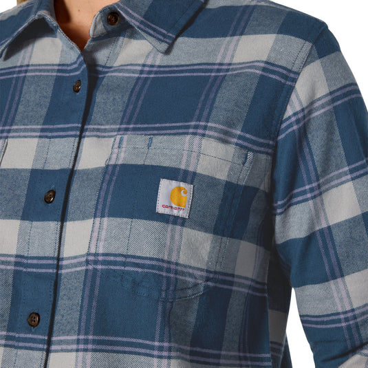 Close-up of a Carhartt plaid button-up shirt in blue, gray, and white, featuring the signature yellow Carhartt logo patch on the chest pocket.