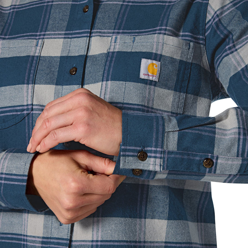 Load image into Gallery viewer, Close-up of a person wearing a blue and gray plaid Carhartt button-up shirt, with both hands adjusting the cuff. The Carhartt logo patch is visible on the chest pocket.
