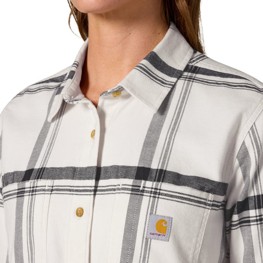 Close-up of a person wearing a Carhartt button-up shirt with a cream base and dark gray plaid stripes. The Carhartt logo patch is visible on the left chest pocket.