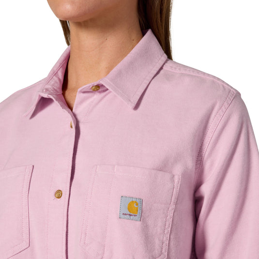 Close-up of a model wearing a light pink Carhartt button-up shirt, showing the collar, front placket, chest pocket, and the Carhartt logo patch on the pocket.