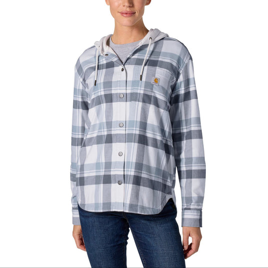 A woman modeling a Carhartt women's hooded button-up shirt in a light blue and gray plaid pattern, paired with dark blue jeans, against a solid white background.