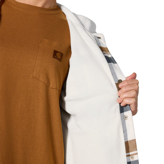 A close-up of a person wearing a brown short-sleeve pocket T-shirt and holding open a white overshirt with a blue, beige, and brown plaid lining. A small brown logo patch is visible on the chest pocket of the shirt.