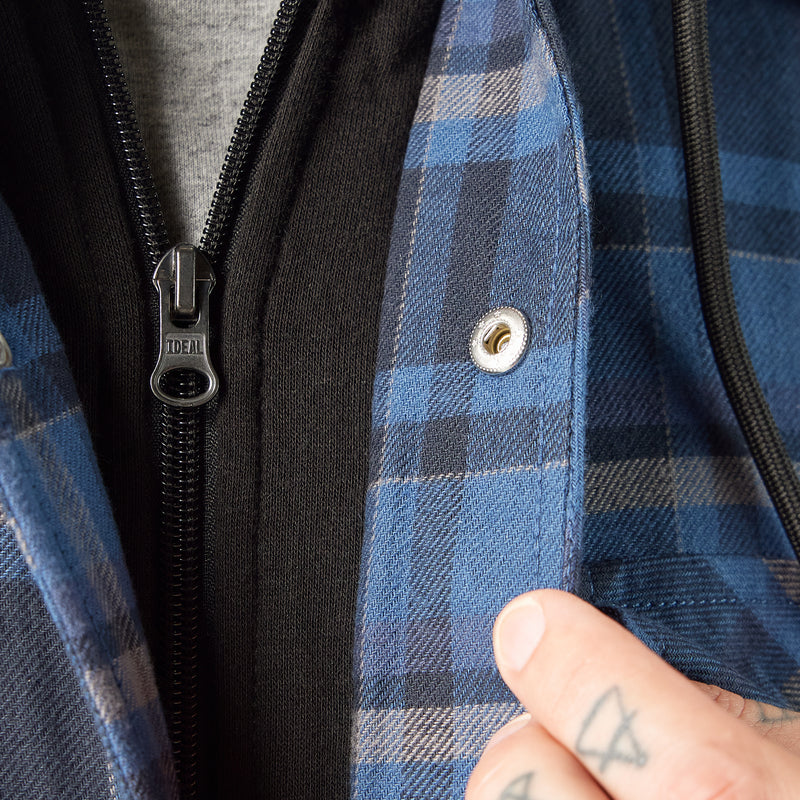Load image into Gallery viewer, Close-up of a blue plaid jacket with a zipper and button, featuring the brand 'Timberland'.

