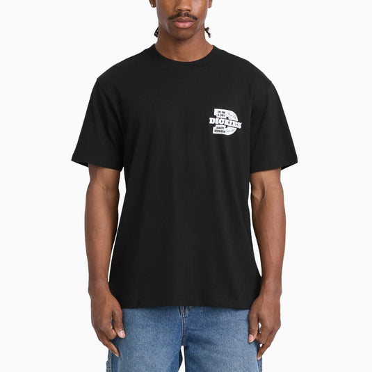 A man wearing a black short-sleeve t-shirt with a small white graphic on the left chest that reads 'DICKIES', paired with blue jeans, against a plain white background.
