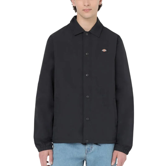 Person wearing a black coaches jacket with a Dickies logo on a white background