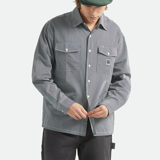 Person wearing a striped shirt with two front button-down flap pockets and a Brixton woven label on the left chest.