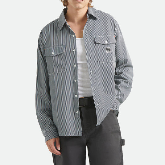 Person wearing a striped shirt with two front button-down flap pockets and a Brixton woven label on the left chest.