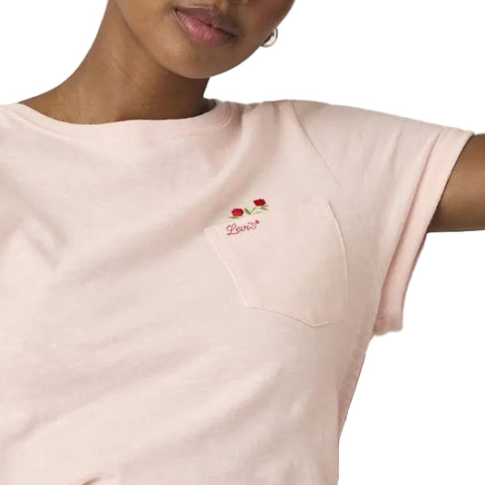 Close up of a wearing a light pink t-shirt with a floral embroidery over the left chest pocket. 