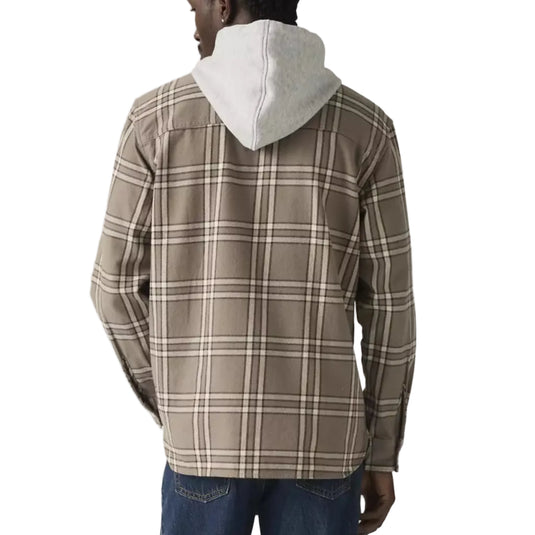 Man wearing a beige plaid shirt over a white t-shirt with a plain background