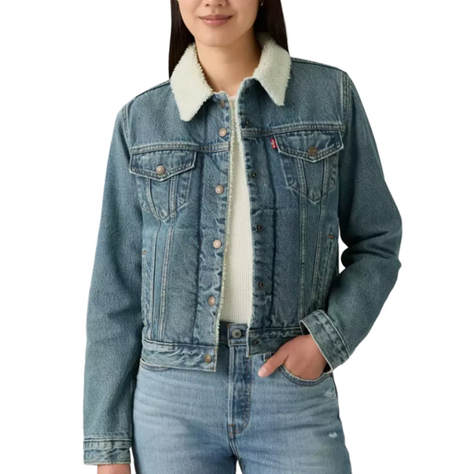 A woman modeling a blue denim jacket with a light beige sherpa collar, paired with matching blue jeans, against a plain light gray studio background.