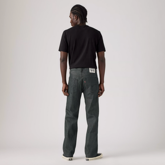 A model shown from the back wearing dark gray straight-leg jeans, a black t-shirt, and black sneakers, standing against a light gray studio background.