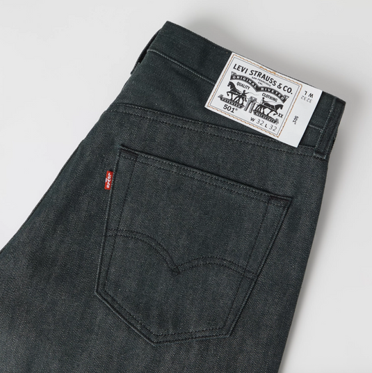 Close-up of the back waistband and pocket area of dark gray Levi's jeans, showing the white Levi's Straws & Co. paper label and the signature red tab.