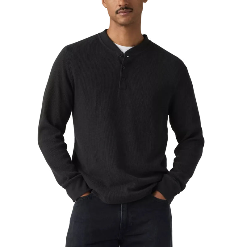 Load image into Gallery viewer, A man wearing a black long-sleeve henley shirt and dark jeans, standing against a light gray studio background.
