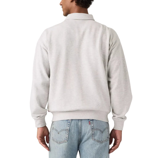A man viewed from behind wearing a light heather gray crewneck sweatshirt and light blue jeans, standing against a solid white studio background.