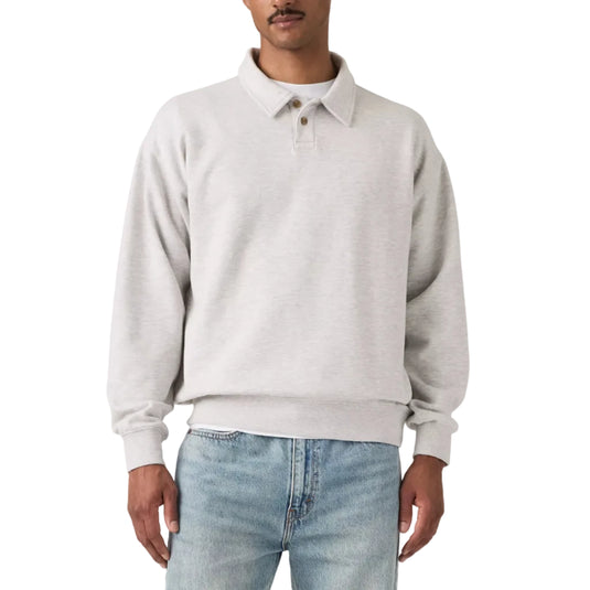 A man wearing a light gray heathered long-sleeve polo sweatshirt and light blue jeans, standing against a neutral light gray studio background.