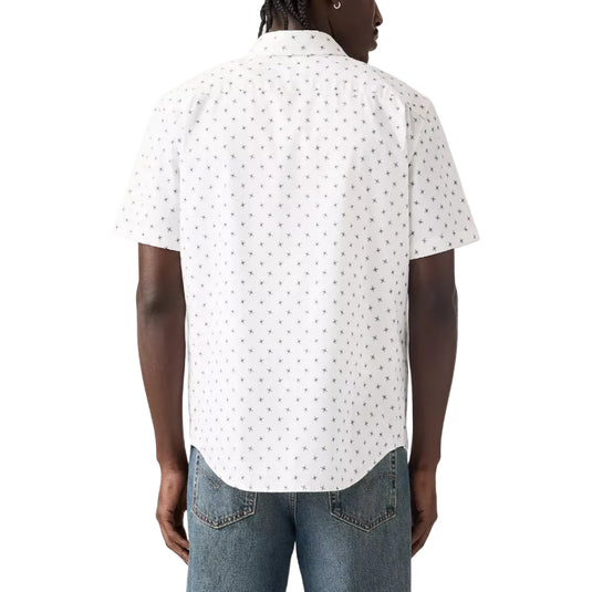 A man viewed from the back wearing a white short-sleeve button-up shirt with a small black geometric pattern, paired with blue jeans, against a light gray studio background.