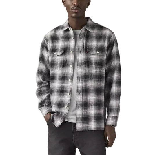 Man wearing a plaid shirt over a white t-shirt with dark jeans on a plain background