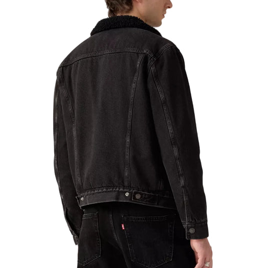 Person wearing a blackish gray denim trucker jacket on a white background
