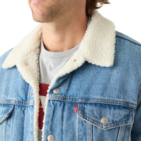 Close-up of a person wearing a light blue denim jacket with a cream sherpa collar over a gray t-shirt. A small red Levi's tab is visible on the chest pocket.