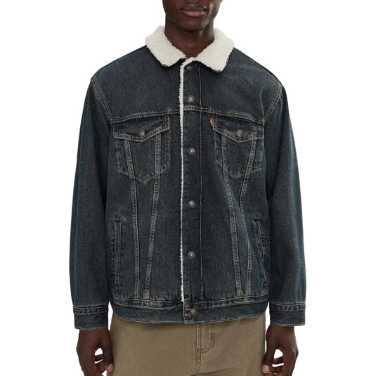 A man wearing a dark blue denim trucker jacket with a white sherpa fleece collar, paired with khaki pants, against a plain white background.