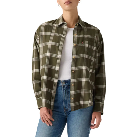A woman modeling an olive green plaid button-up shirt over a white t-shirt and blue jeans, photographed against a neutral light gray studio background.