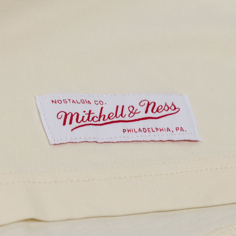 Load image into Gallery viewer, A close-up of a cream-colored fabric label with red embroidered text reading 'Nostalgia Co. Mitchell &amp; Ness Philadelphia, Pa.'
