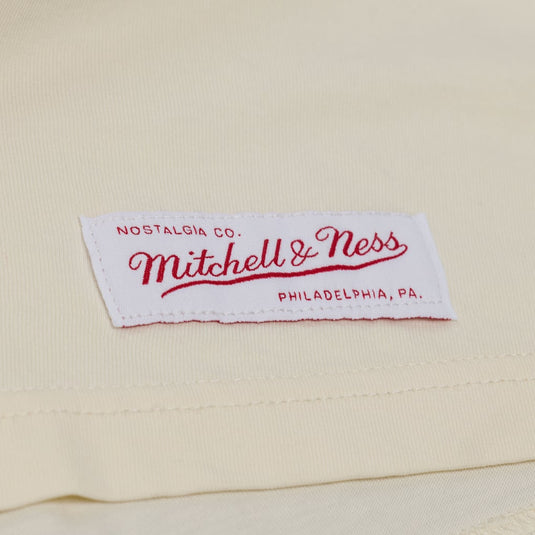 A close-up of a cream-colored fabric label with red embroidered text reading 'Nostalgia Co. Mitchell & Ness Philadelphia, Pa.'