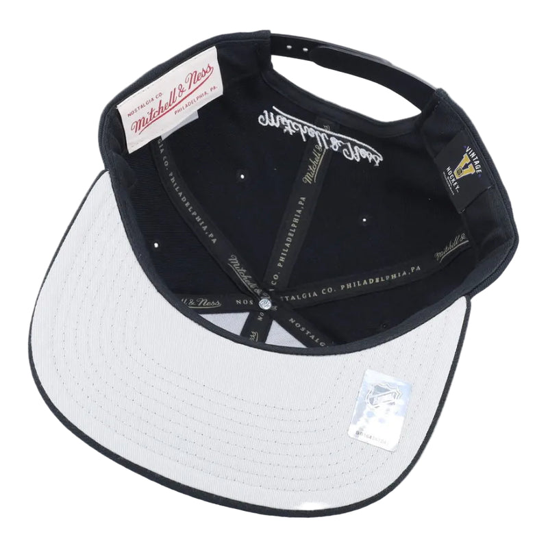 Load image into Gallery viewer, A Mitchell &amp; Ness snapback cap shown from the back, featuring a black crown with white embroidered script and a white visor with black piping.
