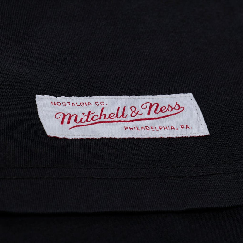 Load image into Gallery viewer, Closeup of the Mitchell &amp; Ness patch sewn into a black tee
