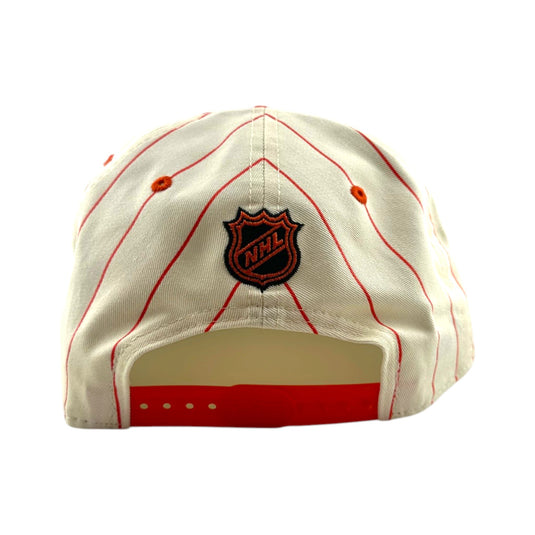 An off-white baseball cap with red pinstripes and an embroidered black and red NHL shield logo on the back, shown against a plain white background.