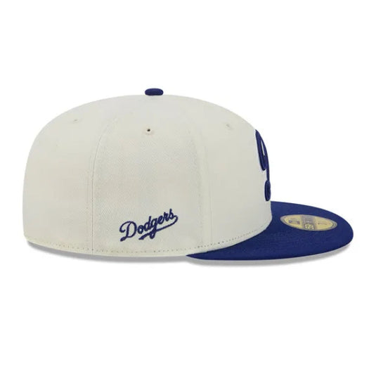 A Los Angeles Dodgers fitted baseball cap in off-white and navy blue, featuring the embroidered 'Dodgers' script on the side and a navy blue 'LA' logo on the front panel.
