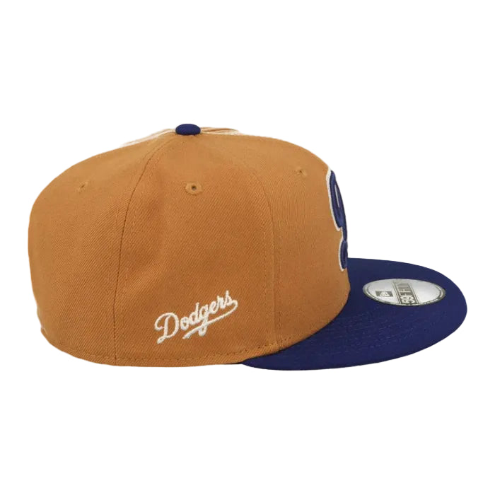 Load image into Gallery viewer, A Los Angeles Dodgers fitted baseball cap in gold and navy blue, featuring a white embroidered 'Dodgers' script on the side and a navy blue 'D' logo on the front panel. The cap has a gold crown, a navy blue flat brim, and a silver metal size sticker on the brim.
