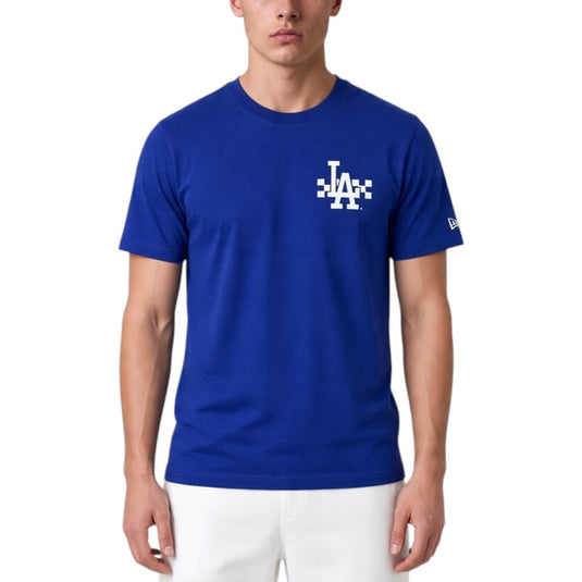 A man wearing a royal blue Los Angeles Dodgers t-shirt with a white graphic logo on the chest, paired with white pants, against a plain white background.