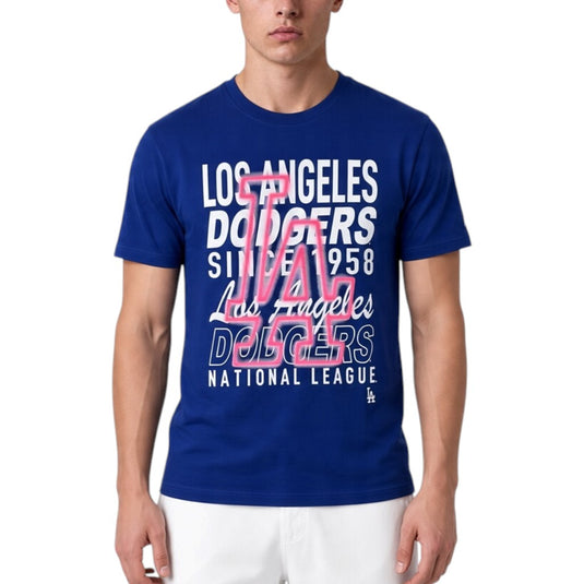 A man wearing a royal blue Los Angeles Dodgers graphic t-shirt with white and pink lettering, paired with white pants, against a plain white background.