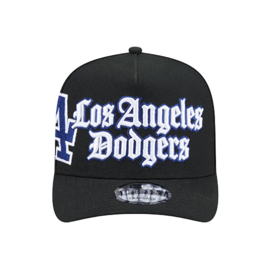 A black baseball cap featuring 'Los Angeles Dodgers' in white Gothic lettering with a blue outline on the front, alongside a blue and white Dodgers 'A' logo on the side. A silver holographic sticker is visible on the brim.