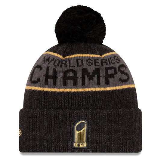 A black knit pom-pom beanie with a gray band reading 'WORLD SERIES CHAMPS' in black and gold stripes, plus a gold championship trophy patch on the cuff.