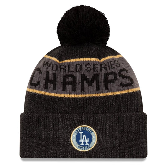 A black knit pom-pom beanie with a gray and gold stripe and 'WORLD SERIES CHAMPS' text, featuring a Los Angeles Dodgers logo patch on the front cuff.