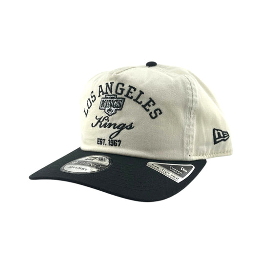 A Los Angeles Kings baseball cap by New Era, featuring an off-white crown with black embroidered lettering and a black curved brim, shown on a plain white background.