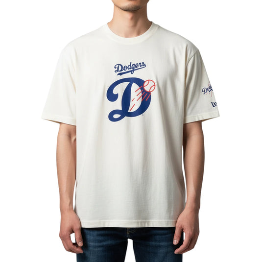 A man wearing a cream-colored Los Angeles Dodgers t-shirt with a blue and red graphic on the front, paired with dark blue jeans, against a plain white background.
