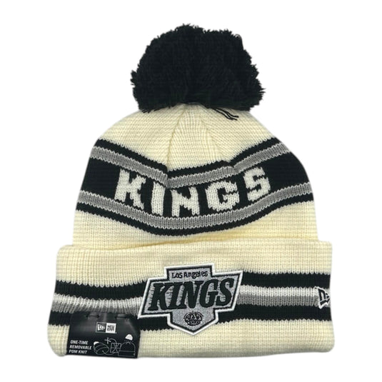A cream and black knit pom-pom beanie featuring the Los Angeles Kings logo and New Era branding.