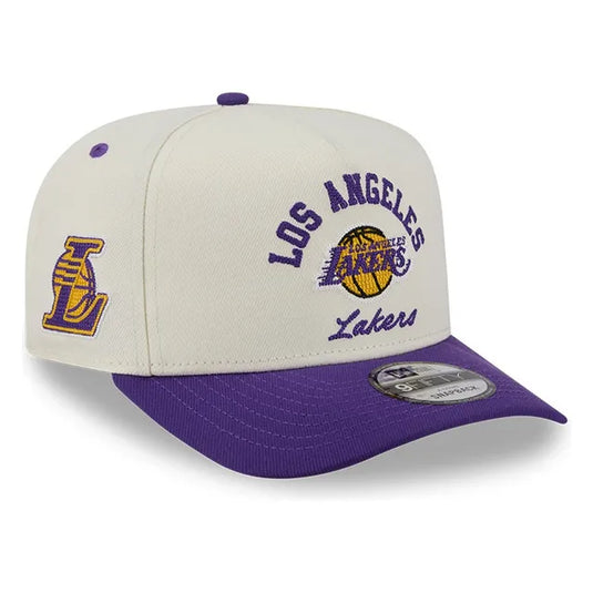 A Los Angeles Lakers New Era 9FIFTY snapback cap in off-white and purple. The front features 'Los Angeles Lakers' embroidered in purple with a yellow basketball logo, and 'Lakers' script below.