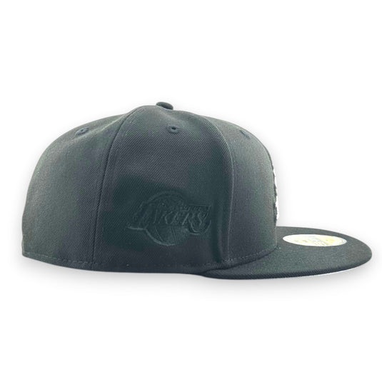 Black cap with a blacked out Lakers logo patc embroidered on the side panel on a white background. 