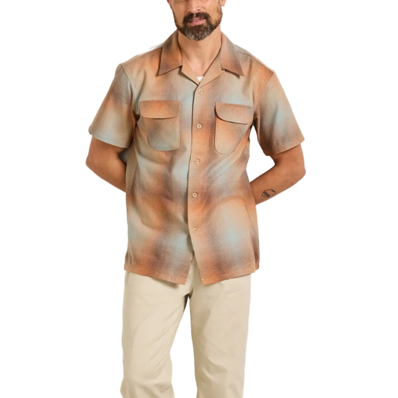 Load image into Gallery viewer, A man modeling a short-sleeve button-up shirt with an abstract painterly pattern in shades of brown, beige, and muted blue, paired with beige trousers and white sneakers against a plain off-white studio background.
